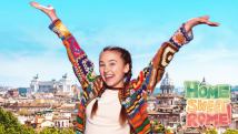 a girl in a colourful sweater raising her arms above her head in front of the skyline of Rome