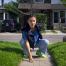 Young girl with vampire teeth sticking out is kneeling on the sidewalk in front of a house
