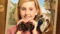 A close-up of a young, blonde girl holding binoculars close to her face, with a dog beside her.